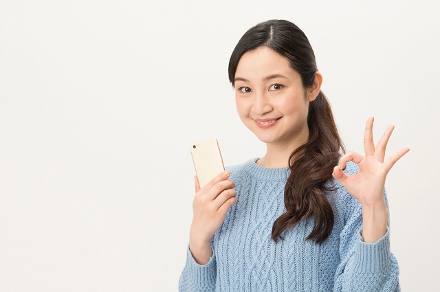 スマホを持ってOKサインをする女性